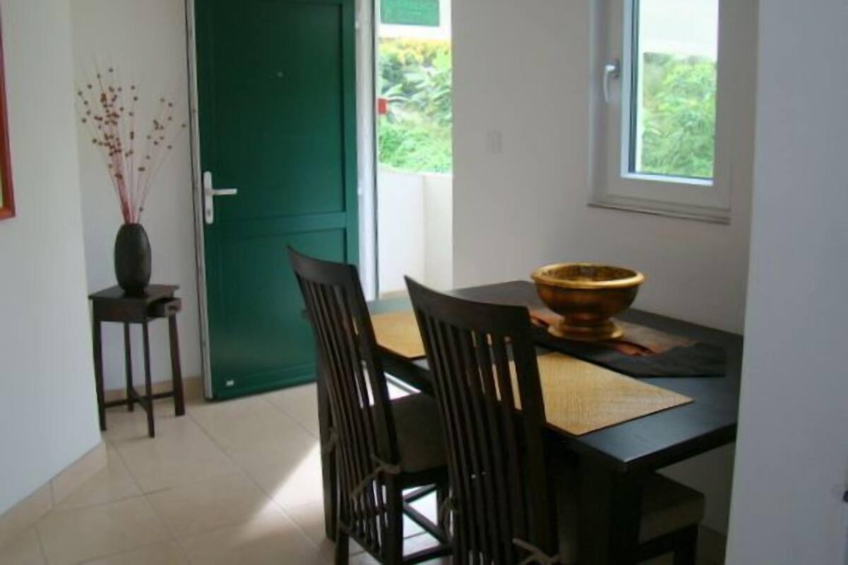 Un comedor con una mesa, sillas, un florero y una puerta verde.