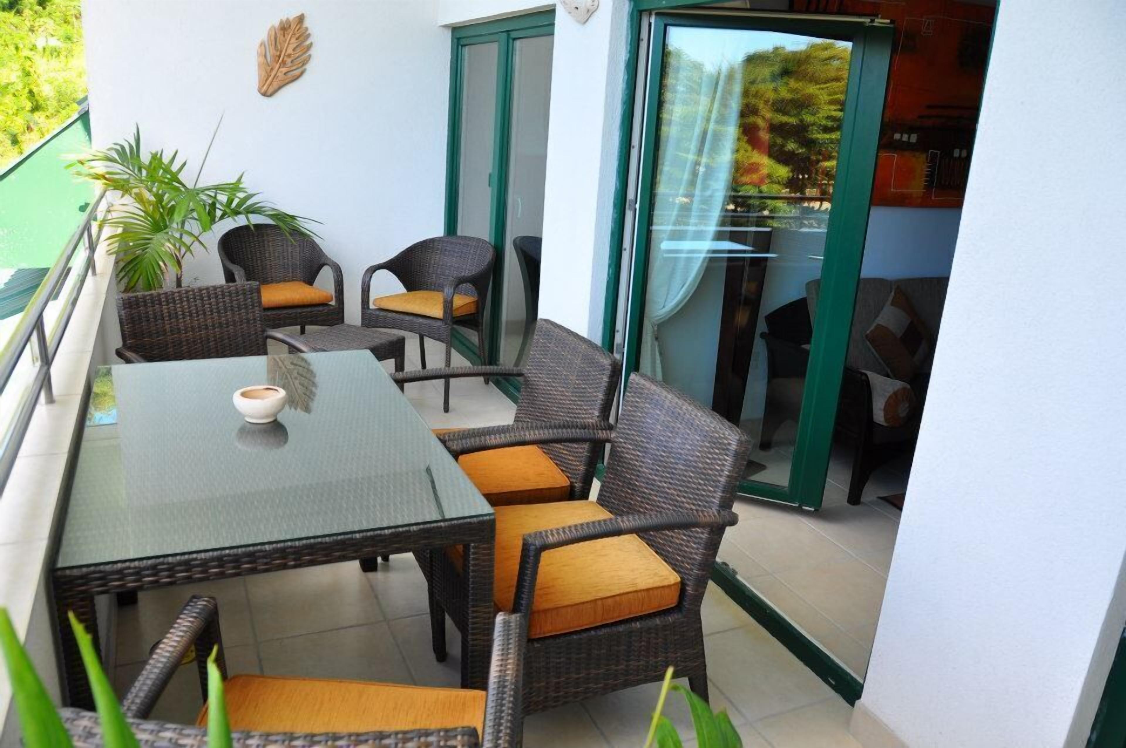 A balcony with wicker furniture, a glass table, and a potted plant.
