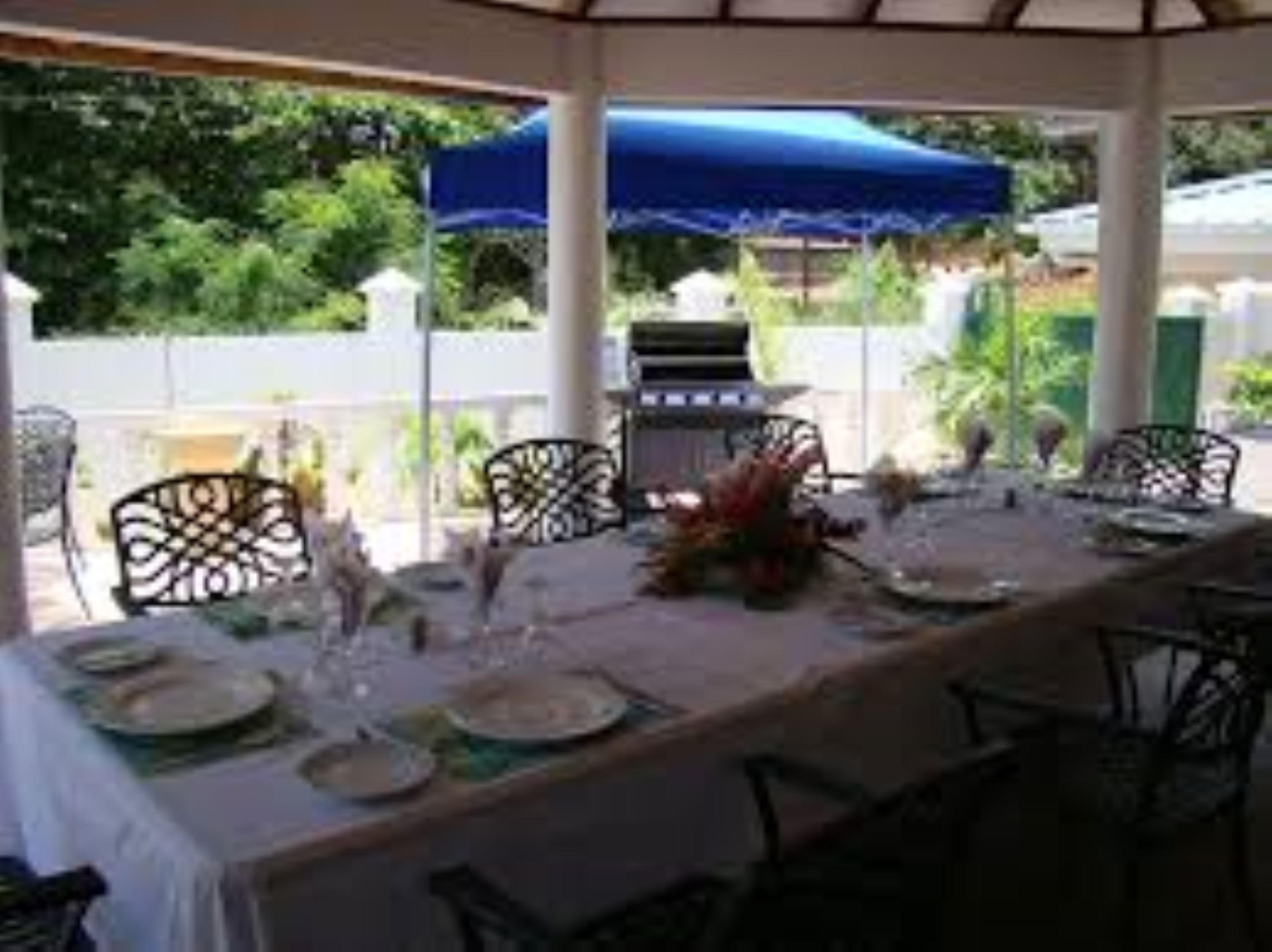An outdoor dining area with a covered table set for four, surrounded by chairs, with a blue canopy overhead.