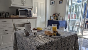 Une table à manger recouverte d’une nappe à motifs, une assiette de nourriture, un verre de jus d’orange et une tasse de café.