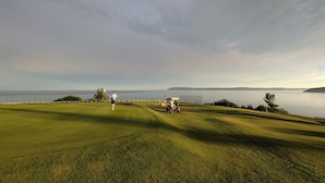 Un parcours de golf offrant une vue sur la mer et les collines lointaines.