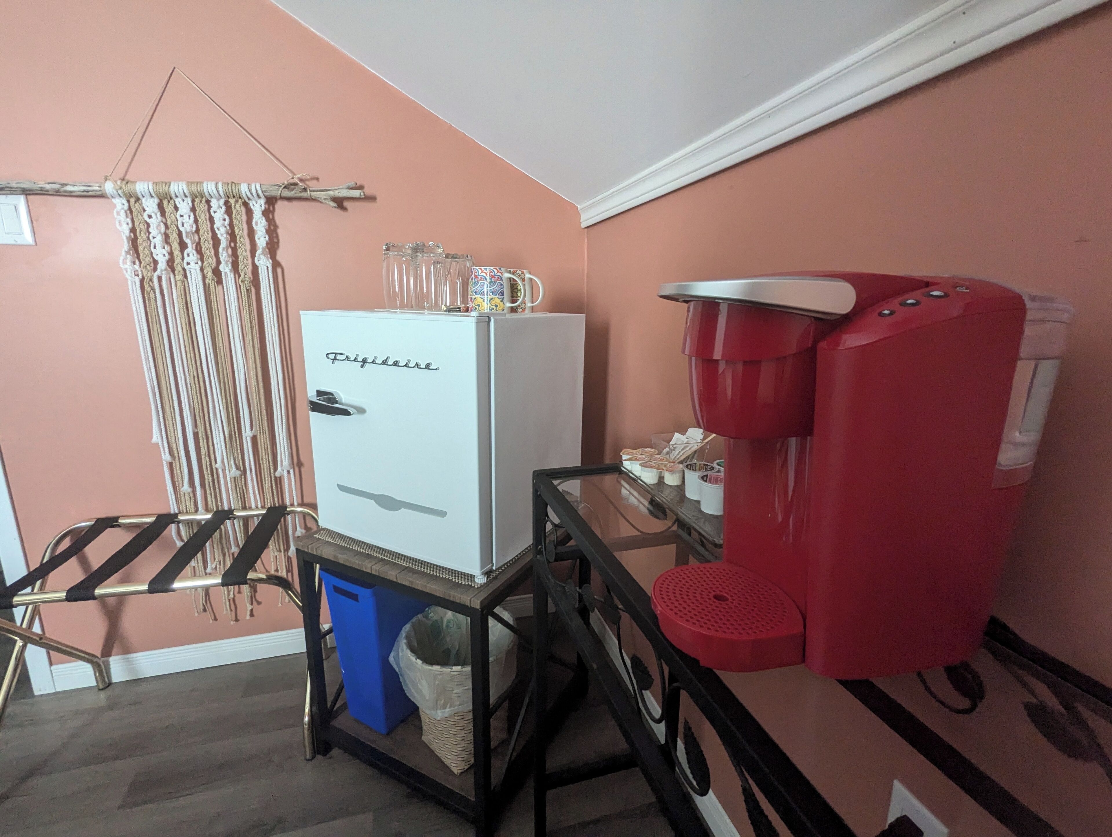 Eine Küchenzeile mit einem weißen Kühlschrank, einer roten Kaffeemaschine, einem kleinen Tisch und einem Hängegestell.