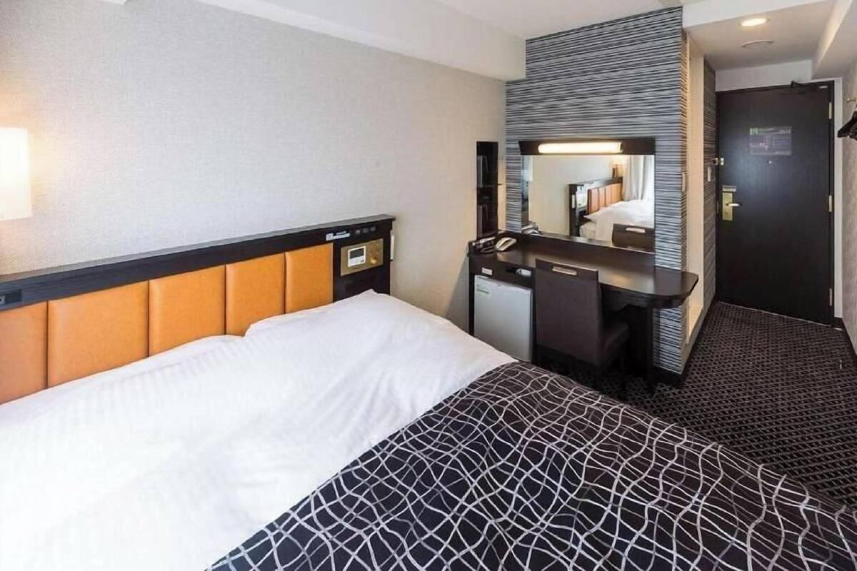 A hotel room with a bed, a desk, a mirror, and a door.
