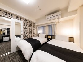 Habitación de hotel con dos camas, un espejo, un escritorio, un armario, un equipo de aire acondicionado y una ventana con cortinas.