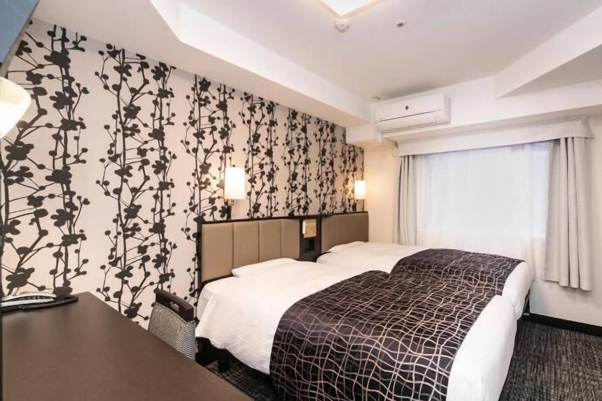 A hotel room with a bed, a desk, a wall-mounted TV, and an air conditioning unit.