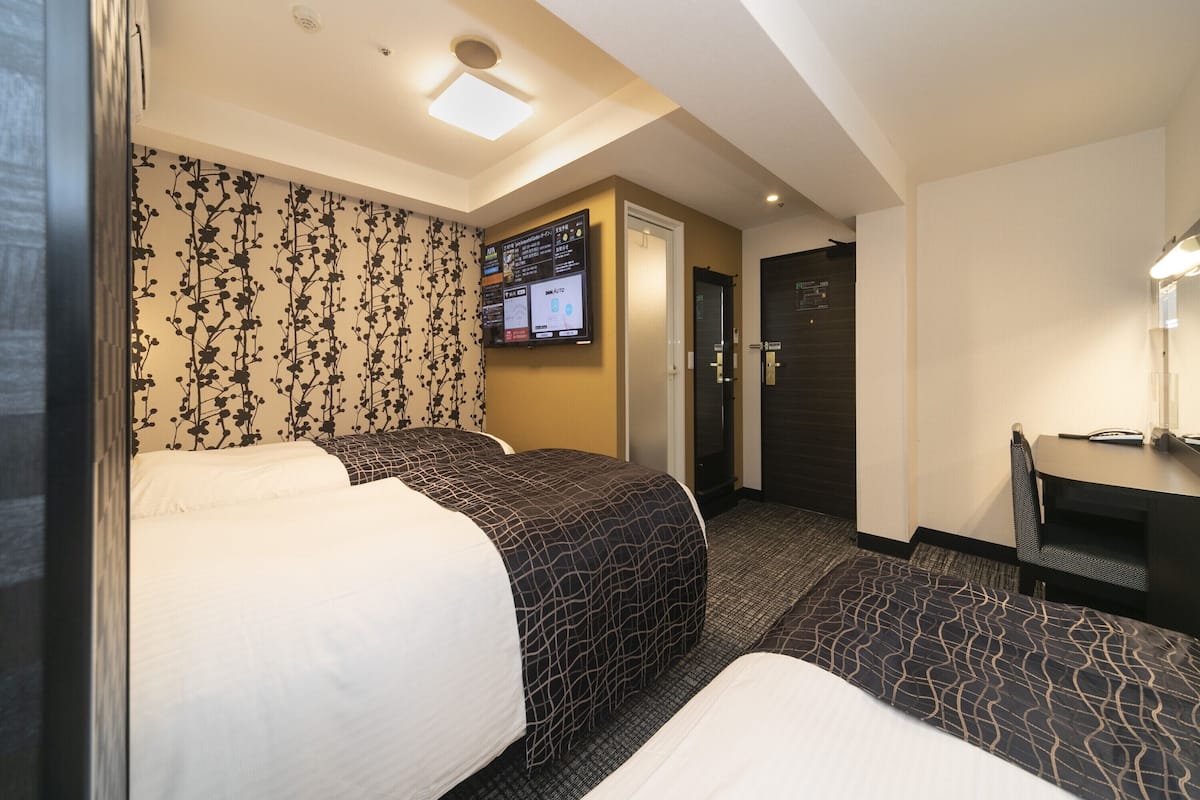 A hotel room with two beds, a desk, a chair, a TV, and a door.