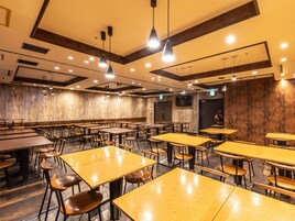 Un comedor amplio con varias mesas y sillas, paredes de madera e iluminación colgante.