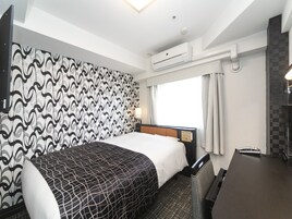 Habitación de hotel con cama, escritorio, silla, equipo de aire acondicionado y ventana con cortinas.