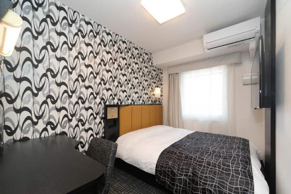 Habitación de hotel con cama, escritorio, silla, pared con estampado, televisión y equipo de aire acondicionado.