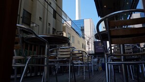 Vista de un edificio con una torre, zona de estar al aire libre con sillas metálicas y un letrero que dice APA Villa Hotel.