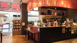 Interior de una cafetería con mostrador, carteleras del menú y exhibición de artículos relacionados con el café.
