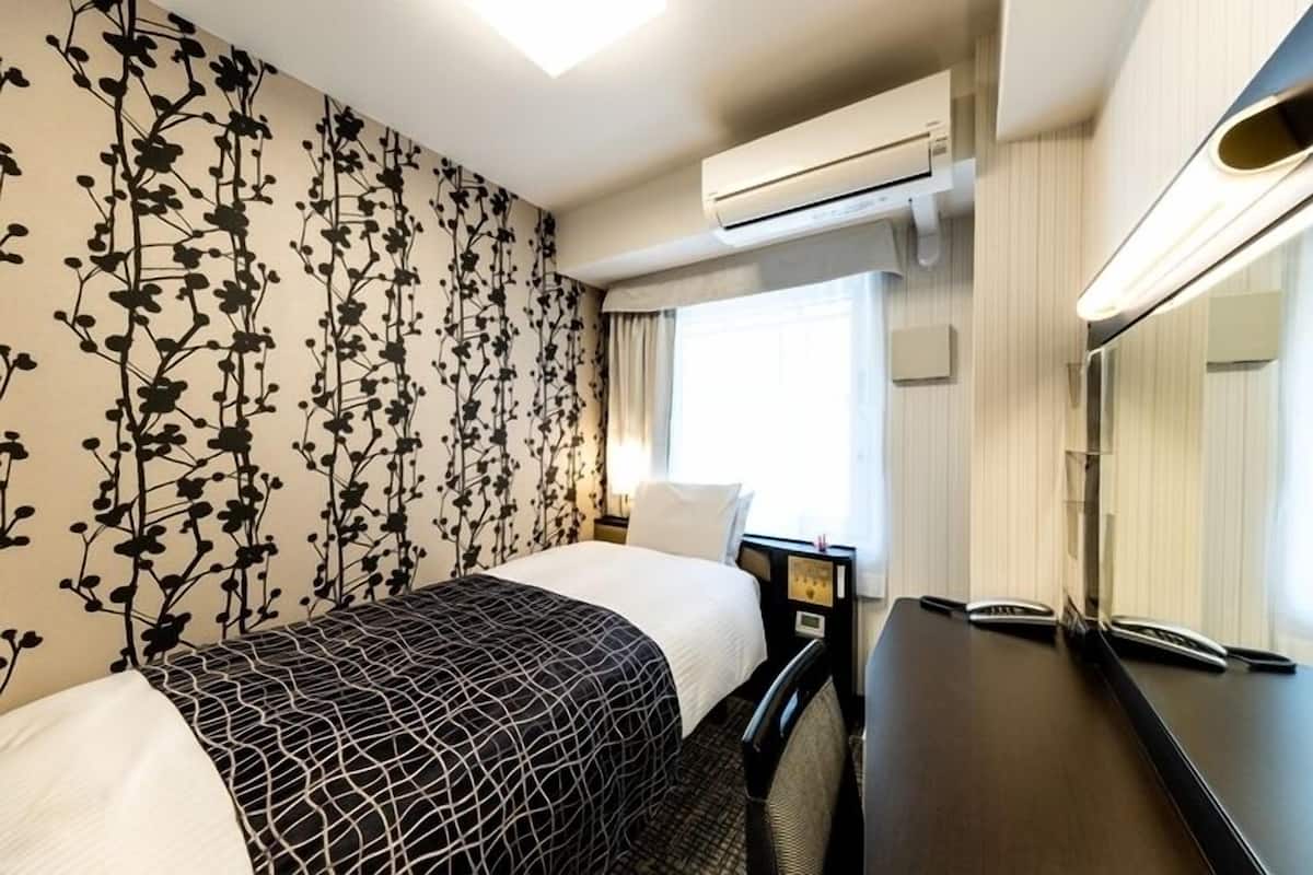 Quarto de hotel com cama, secretária, telefone, ar condicionado e janela com cortinas.