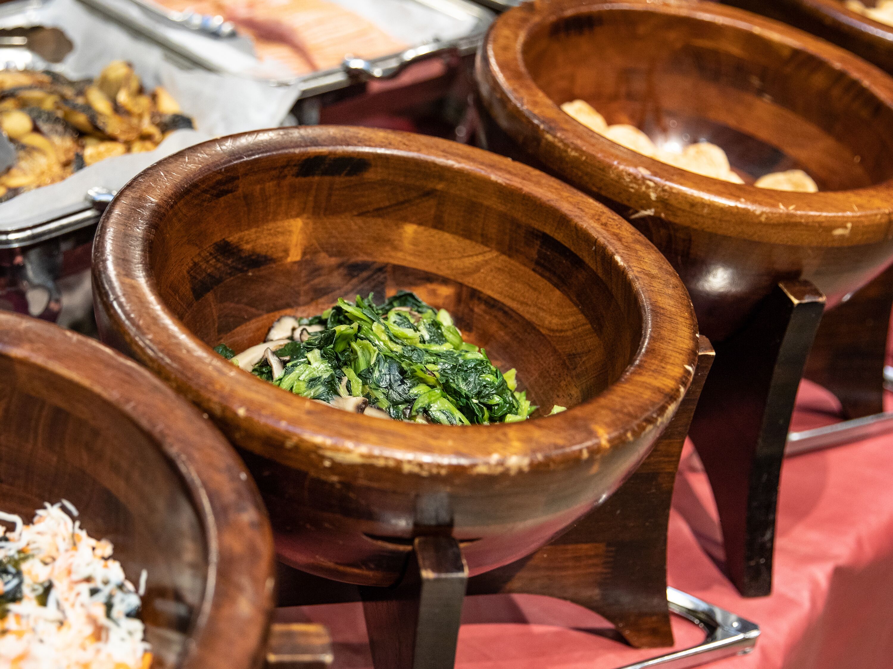 A buffet with various dishes, including a bowl of greens and other food items.