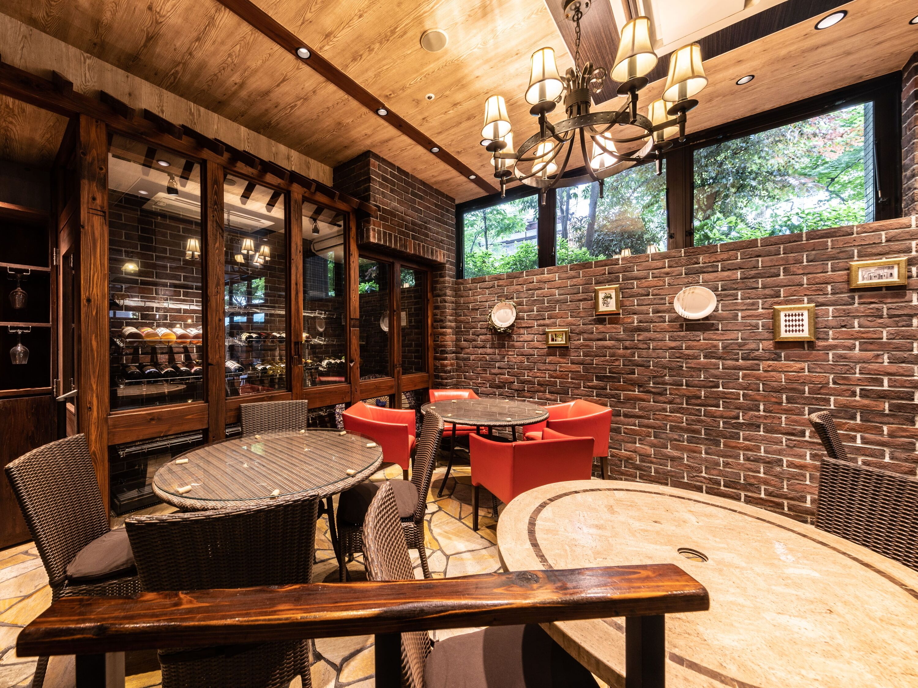 Un acogedor interior de restaurante con paredes de ladrillo, vigas de madera en el techo y diferentes opciones de asientos, incluyendo mesas redondas y sillas rojas.
