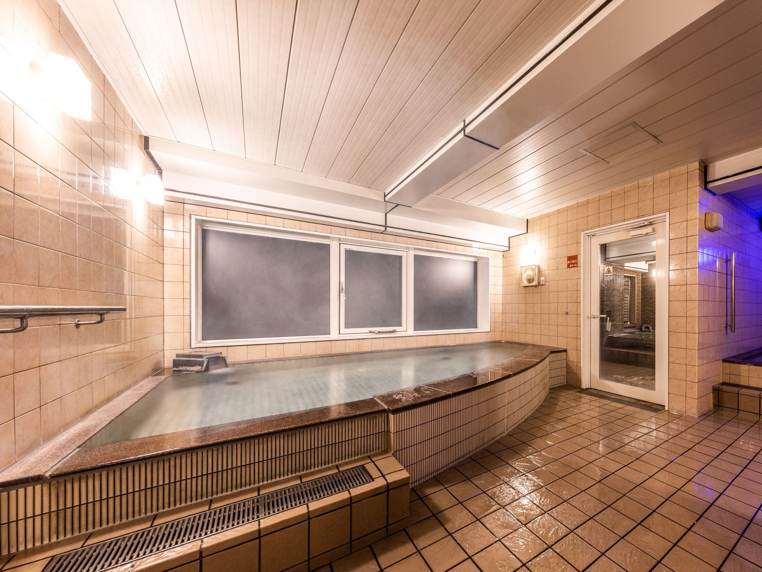 A modern bathroom with a large bathtub, tiled walls, and a ceiling with linear lighting.