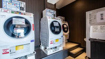 A laundry facility with multiple washing machines and dryers, equipped with instructional signs and safety warnings.