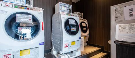 A laundry facility with multiple washing machines and dryers, equipped with instructional signs and safety warnings.