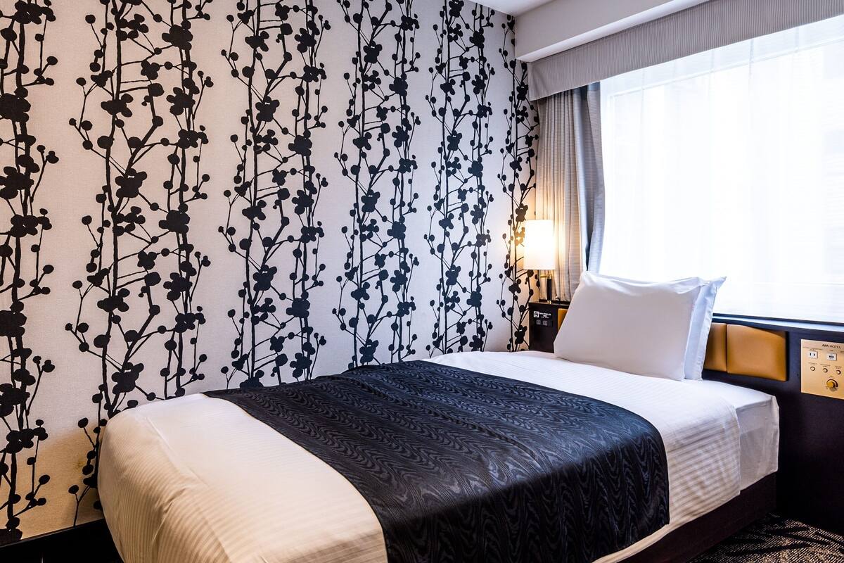 Ein Hotelzimmer mit Bett, Nachttisch, Lampe und einem Fenster mit Vorhängen.