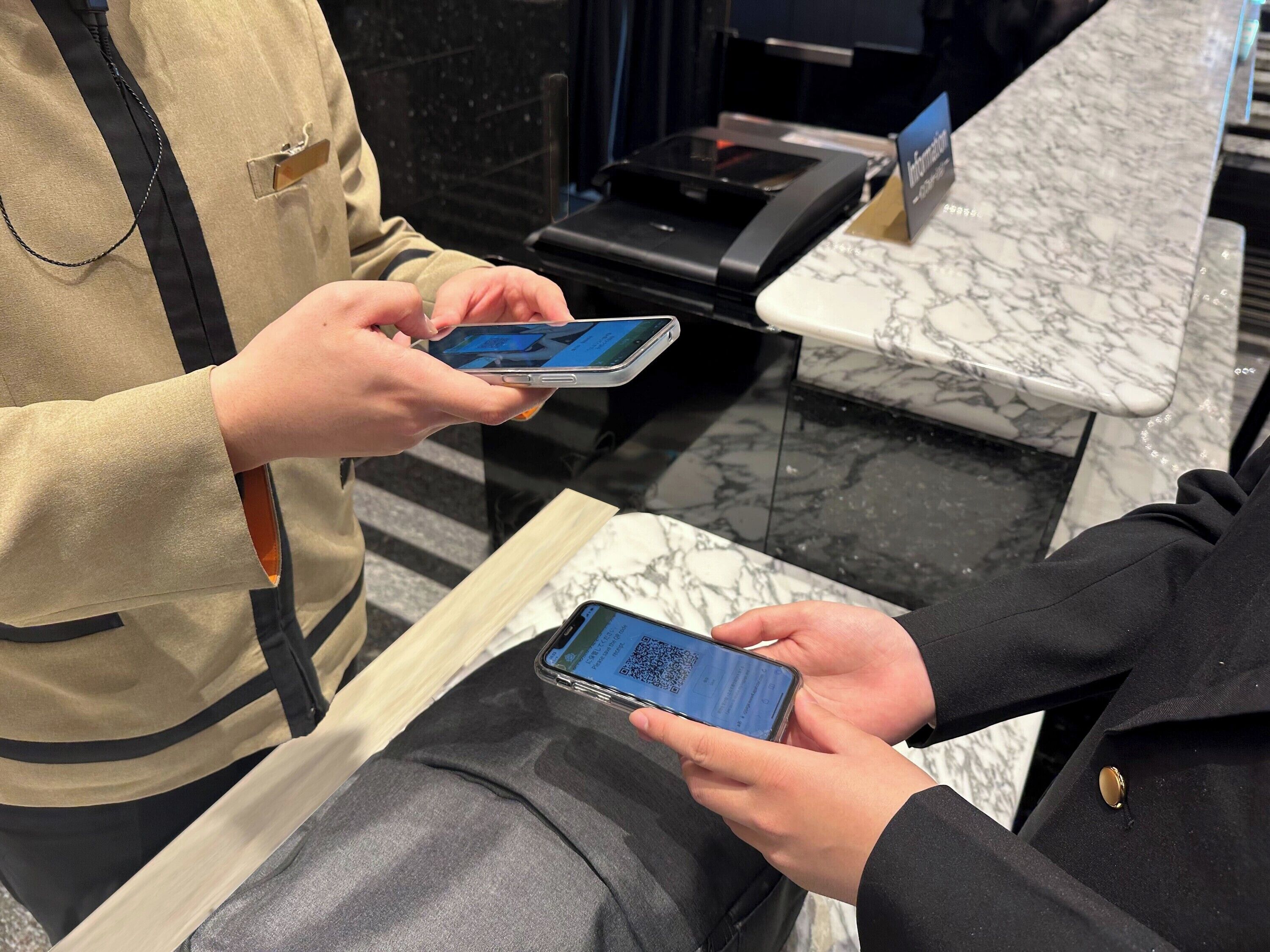 A person holding a smartphone with a QR code, standing next to a counter with a marble surface.