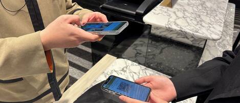 A person holding a smartphone with a QR code, standing next to a counter with a marble surface.