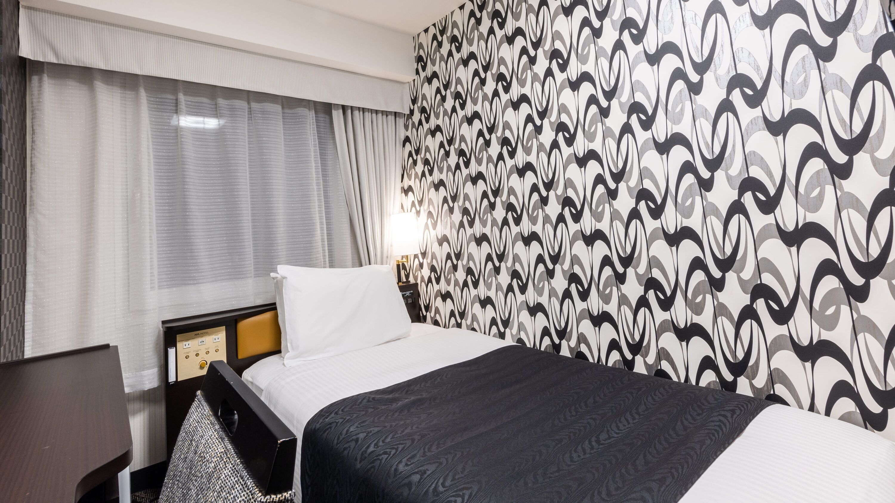 A hotel room with a bed, a desk, and a patterned wall.