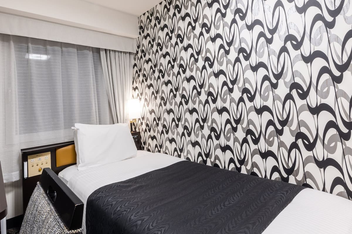 A hotel room with a bed, a desk, and a patterned wall.