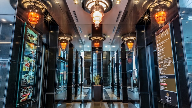 A modern hotel lobby with a central chandelier, glass walls, and a digital menu display.