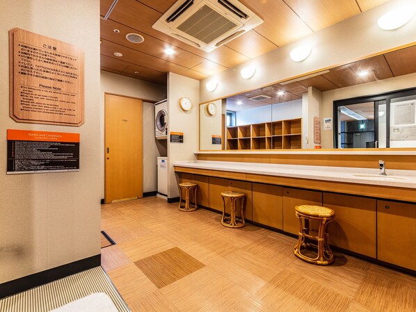 A hotel restroom with a wooden floor, a sink, a mirror, and two stools. There are signs on the wall with instructions and terms. - APA Hotel Osaka Higobashi Ekimae Tower (Osaka)
