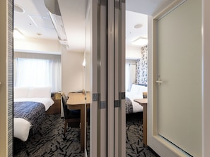 Quarto de hotel com cama, escrivaninha, cadeira e porta.