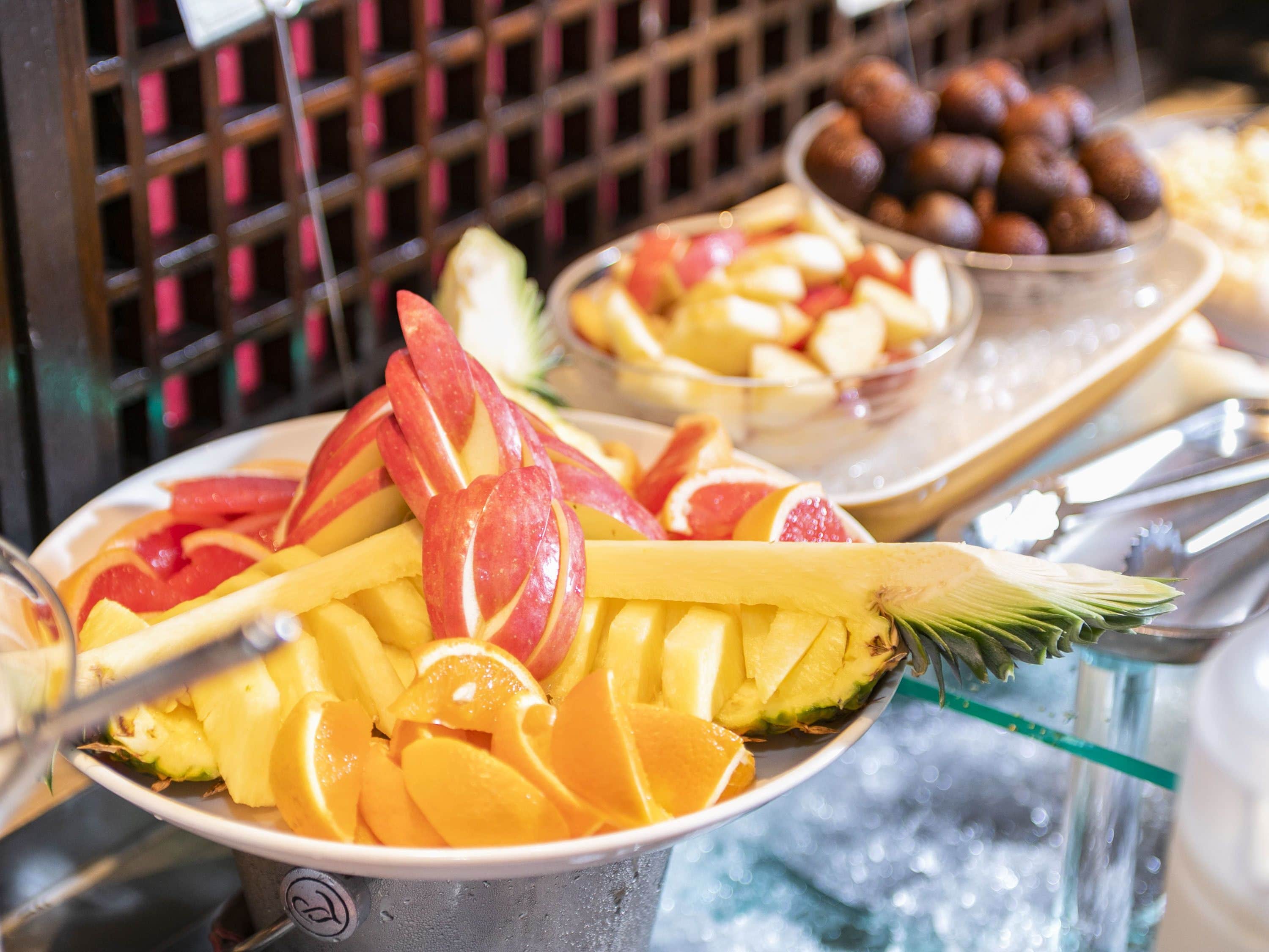 Un présentoir rempli de différents fruits, comme des pommes, des oranges et des mangues.