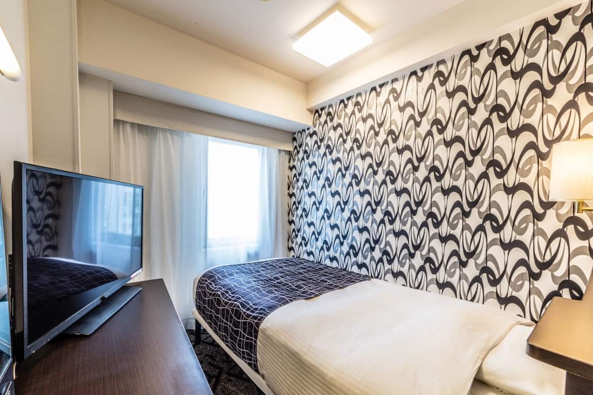 Habitación de hotel con cama, escritorio con televisor, ventana con cortinas y pared con diseño.