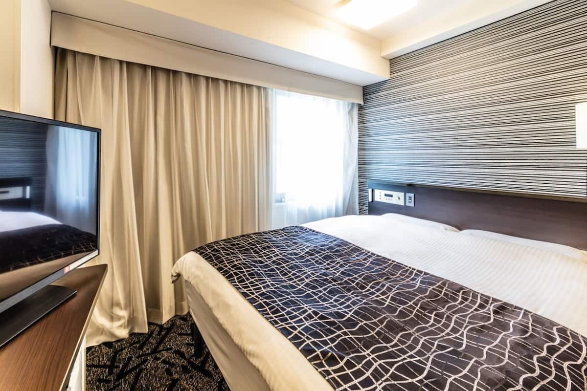 Una habitación de hotel con cama, televisor y ventana con cortinas.
