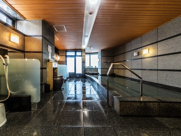 Un área de piscina interior moderna con pared de vidrio, techo de madera y suelo de baldosas.