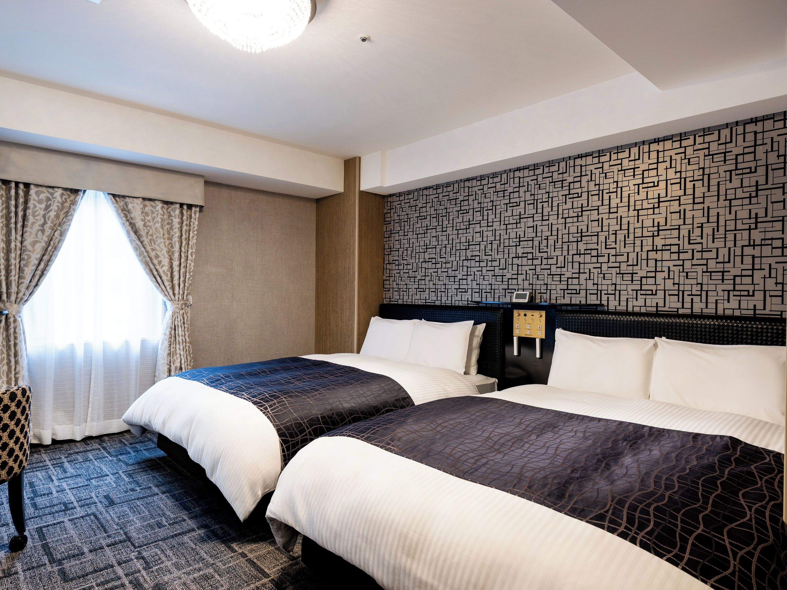 A hotel room with two beds, a patterned wall, and a window with curtains.