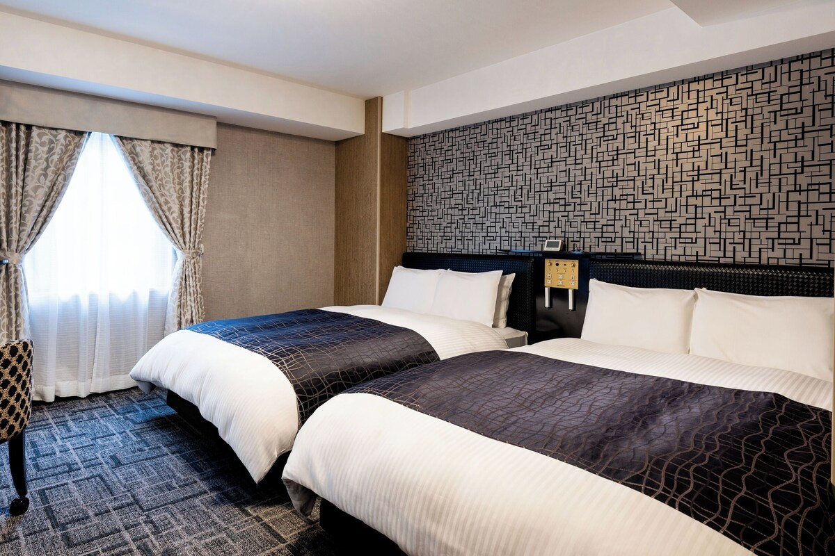 Habitación de hotel con dos camas, un papel tapiz estampado y una ventana con cortinas.