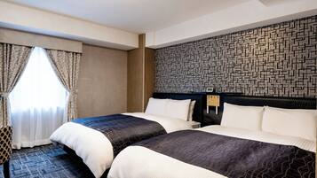 A hotel room with two beds, a patterned wall, and a window with curtains.