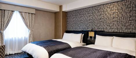 A hotel room with two beds, a patterned wall, and a window with curtains.