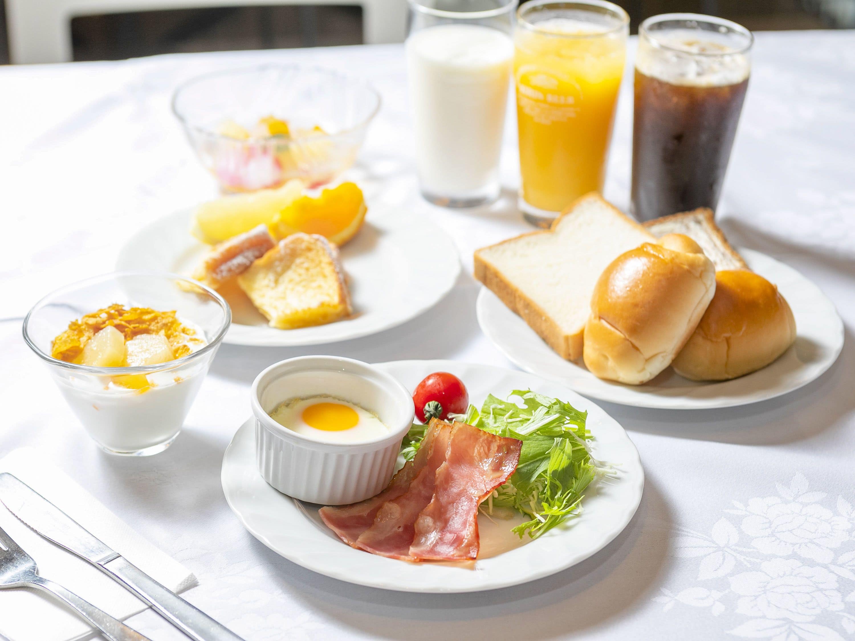 A breakfast setting with plates of toast, eggs, ham, and salad, along with glasses of milk and orange juice.
