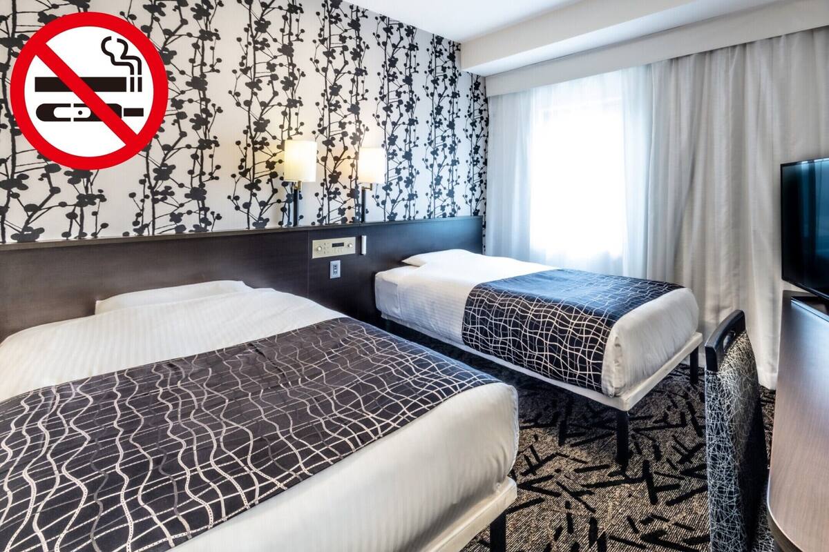 Habitación de hotel con dos camas, un televisor y un cartel de no fumar.