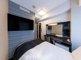Una habitación de hotel moderna con una cama grande, un escritorio con espejo, un televisor de pantalla plana y un cubo de basura pequeño.