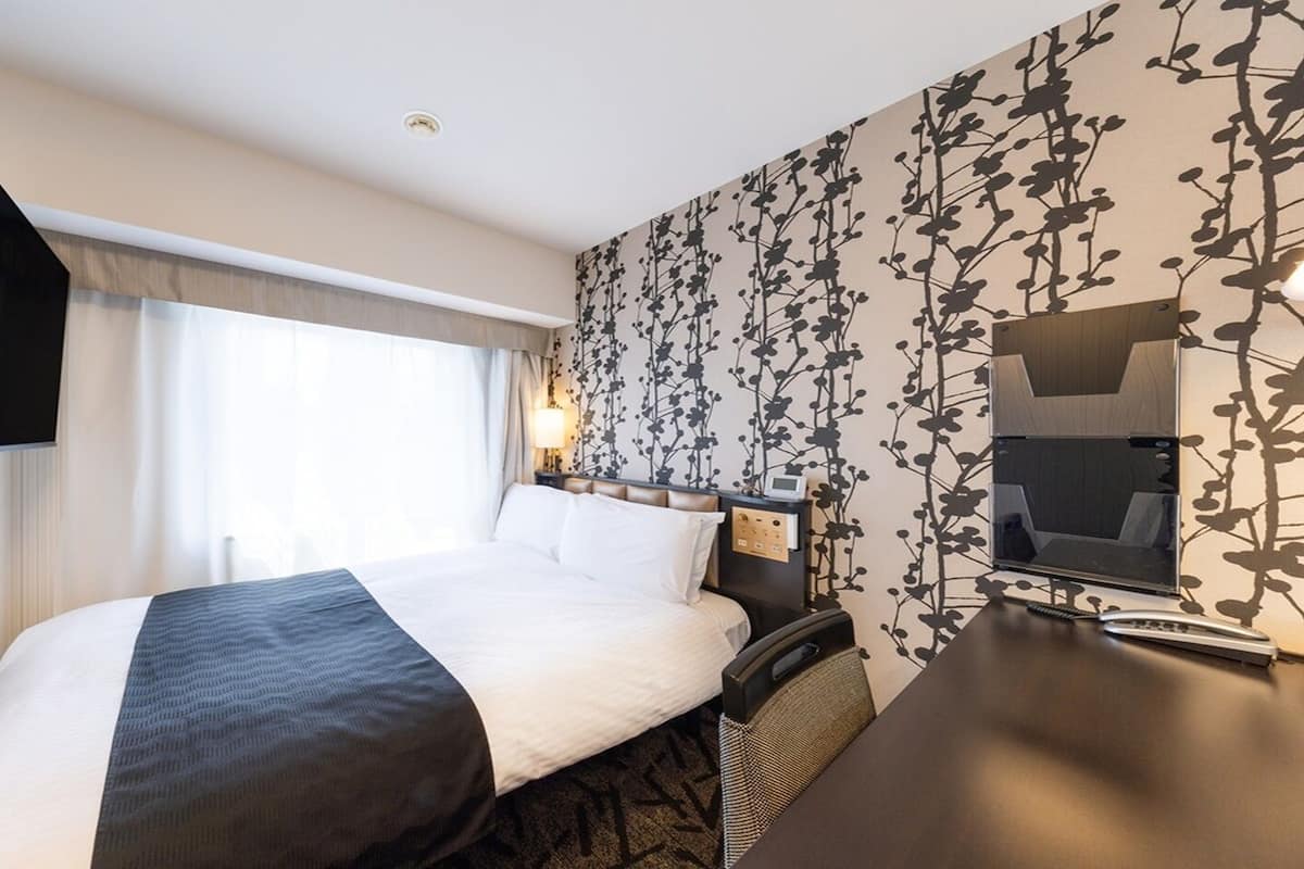Ein Hotelzimmer mit einem Bett, einem Schreibtisch, einem Fernseher und einer Wand mit einem Blumenmuster.