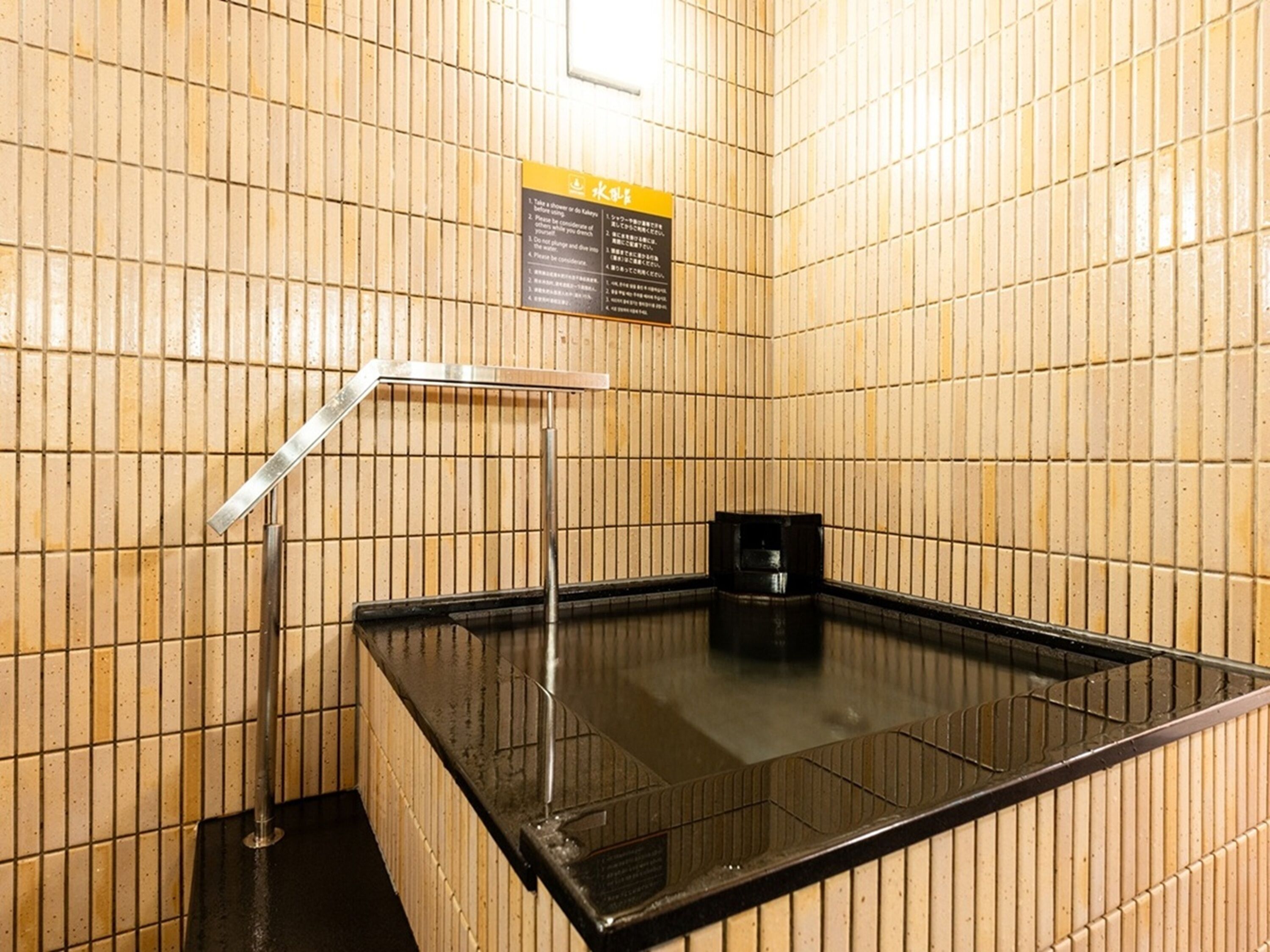 Een sauna met betegelde wanden, een hottub in een glazen hoes en een zwarte heater.