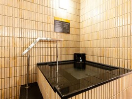 A sauna room with tiled walls, a glass-enclosed hot tub, and a black heater.