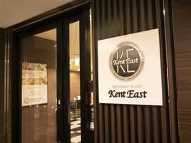 Un letrero de restaurante con el texto 'Kent East' y 'RESTAURANT & CAFE', un menú y una puerta con un reflejo.
