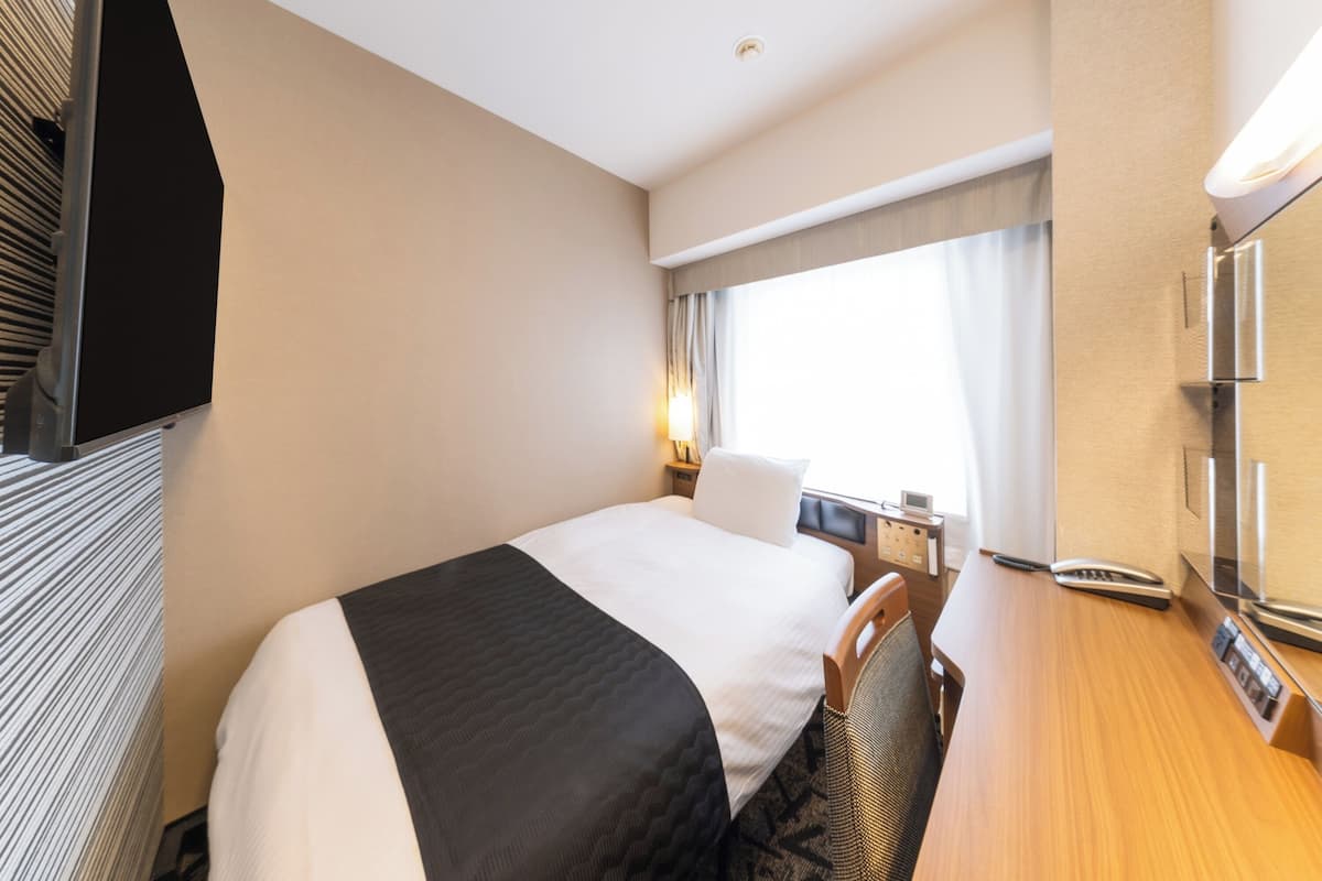 A hotel room with a bed, a desk, a chair, a TV, and a window with curtains.