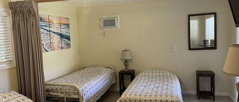 A room with two single beds, a ceiling fan, a painting, a mirror, and a window with curtains.