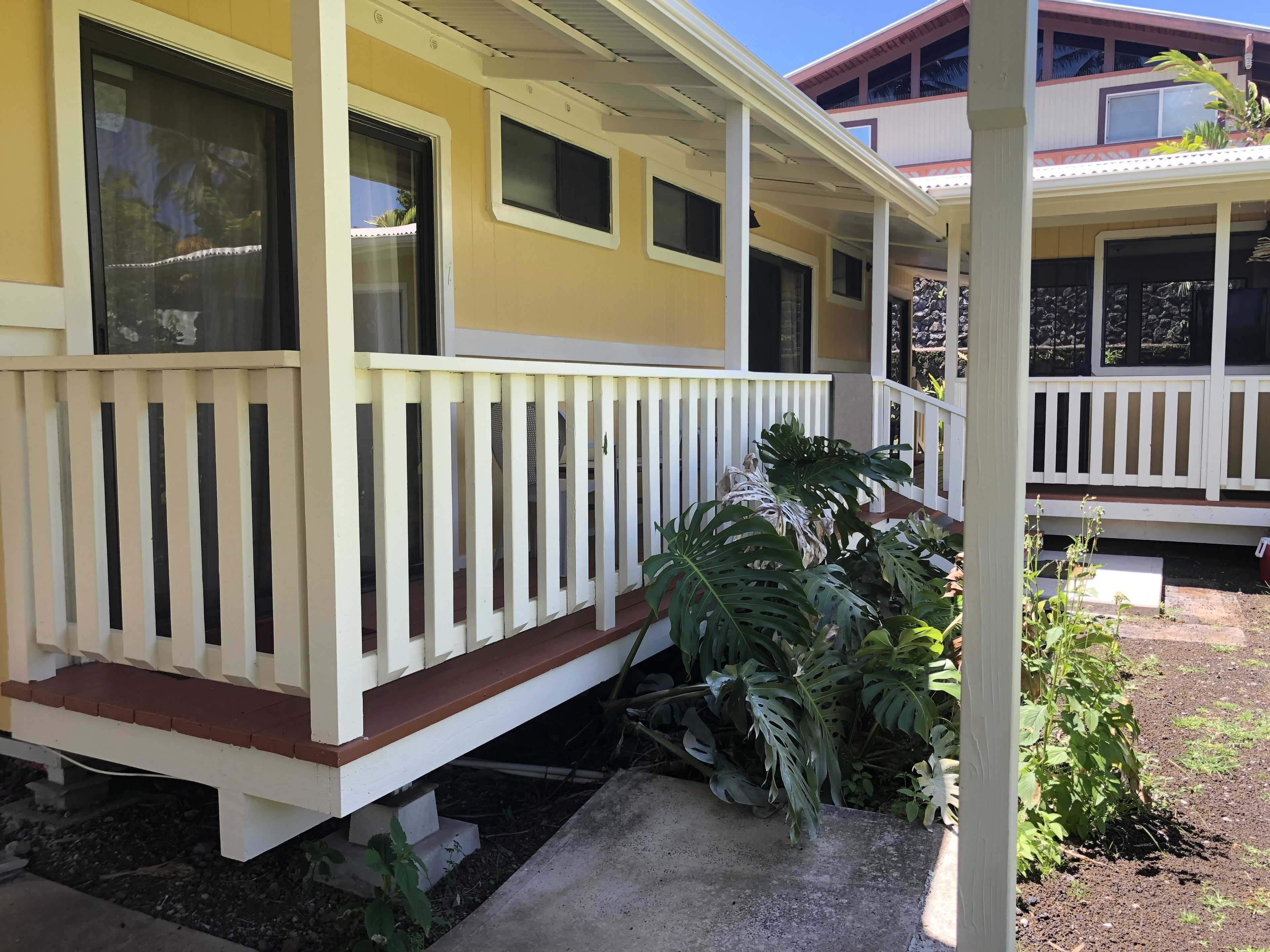 A yellow building with a white porch and a small garden area.