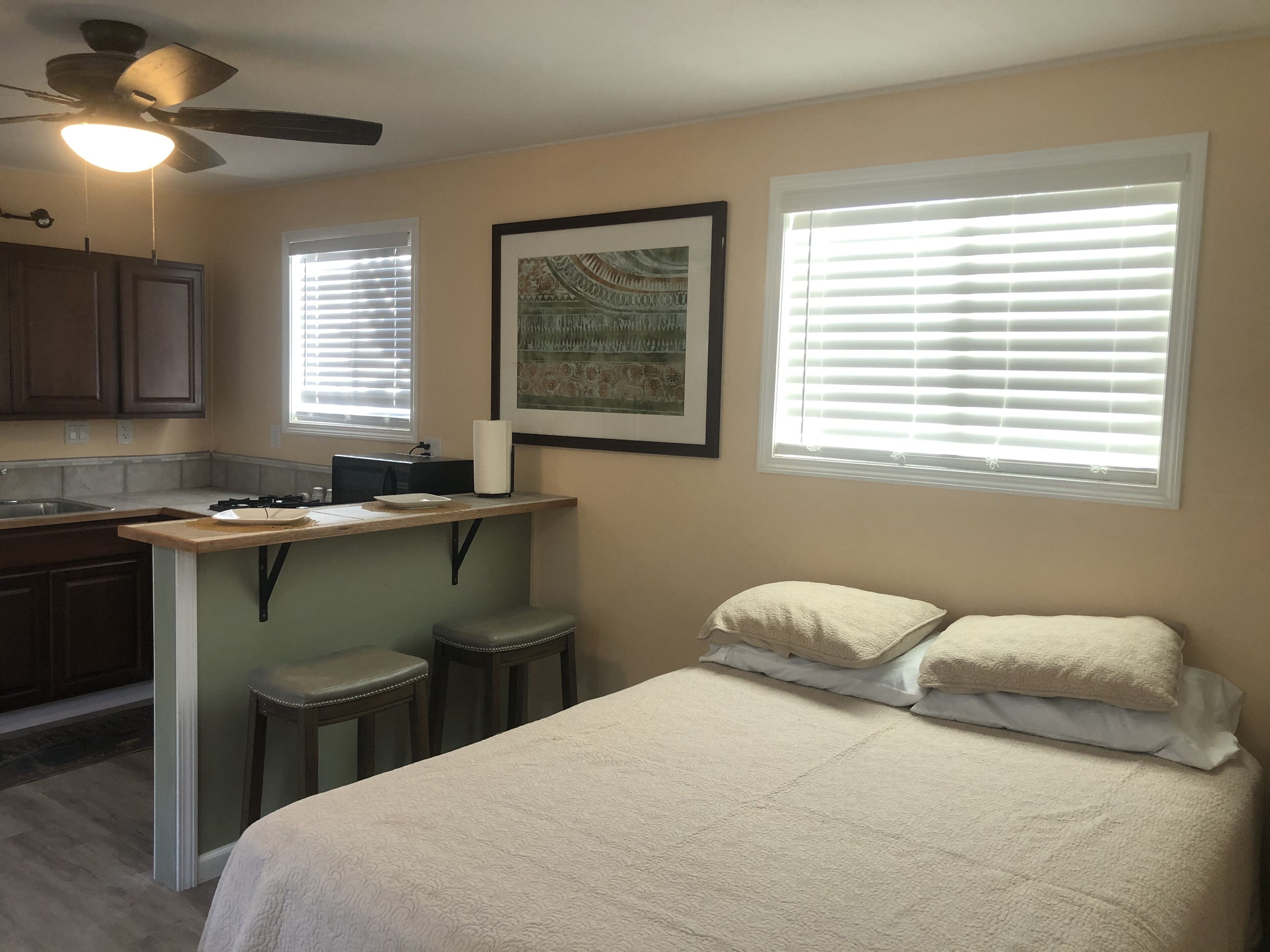 Une chambre compacte comprenant un lit, un petit coin cuisine et un ventilateur de plafond.