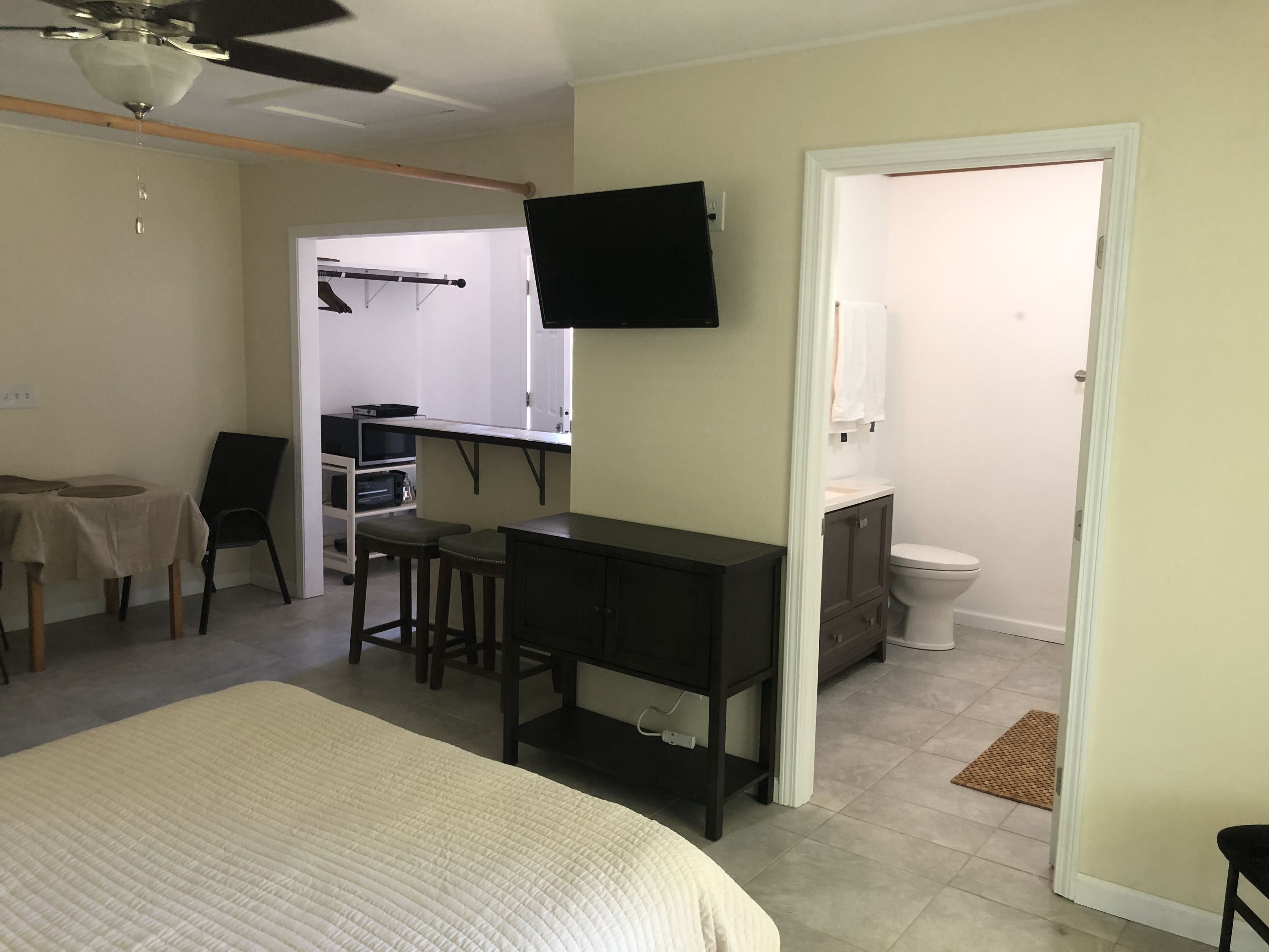 A bedroom with a bed, a desk, a chair, a TV, and a bathroom visible through an open door.