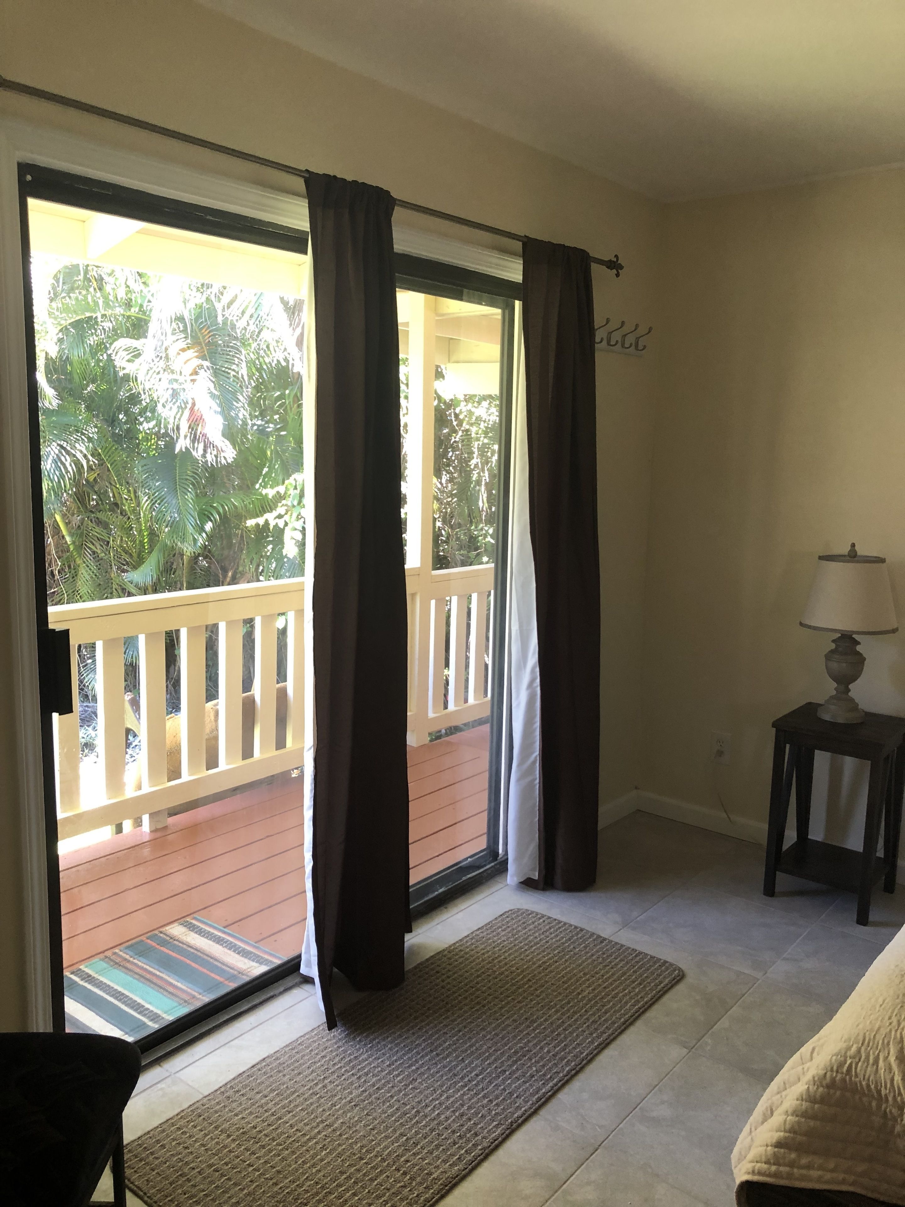 A room with a sliding glass door leading to a balcony, a small table with a lamp, and a doormat.